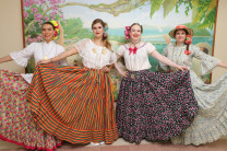 Las estudiantes mostrando la belleza de las polleras. Cuatro estudiantes de intercambio vestidas con polleras panameñas frente a un mural con paisajes naturales.