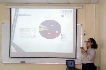 Karina García, en el aula de sustentación presentando un PowerPoint, en una pantalla..
